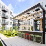 Bar with seats outside surrounded by several floors of a multifamily apartment complex.
